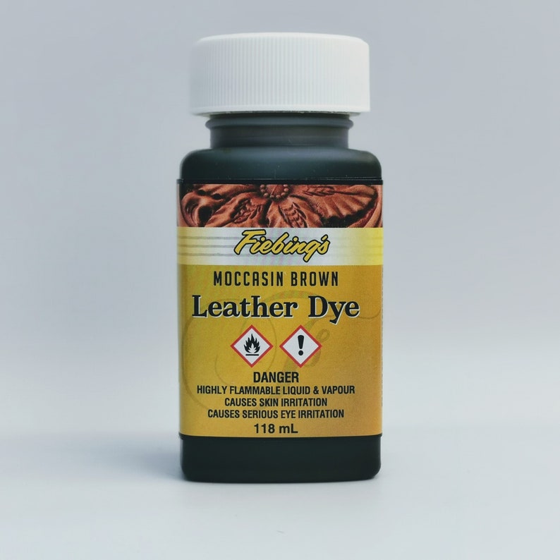 May include: A small bottle of Fiebing's Leather Dye in Moccasin Brown. The bottle is black with a yellow label and a white cap. The label has a warning that the liquid is highly flammable and causes skin and eye irritation. The bottle contains 118 ml of dye.