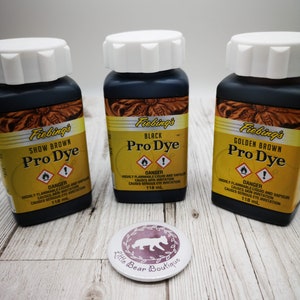 May include: Three glass bottles of Fiebing's Pro Dye leather dye. The bottles are labeled with the colors: Show Brown, Black, and Golden Brown. Each bottle contains 118 ml of dye.