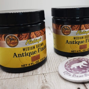 May include: Two 118ml bottles of Fiebing's Medium Brown Antique Finish leather dye. The bottles have a yellow label with black text and a brown background.
