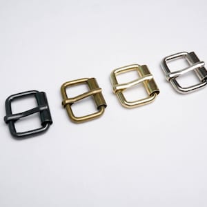 May include: Four metal belt buckles in different finishes: black, brass, gold, and silver. Each buckle has a rectangular shape with a curved, smooth bar.