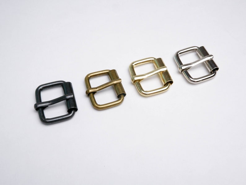 May include: Four metal belt buckles in different finishes: black, brass, gold, and silver. Each buckle has a rectangular shape with a curved, smooth bar.