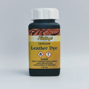 May include: A black bottle of Fiebing's Cordovan Leather Dye with a white cap. The bottle is labeled with a yellow warning label that reads "DANGER: HIGHLY FLAMMABLE LIQUID & VAPOUR CAUSES SKIN IRRITATION CAUSES SERIOUS EYE IRRITATION 118 mL".