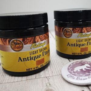 May include: Two 118ml bottles of Fiebing's Light Brown Antique Finish leather dye. The bottles are on a light wood surface with a small round sticker that says "Little Bear Boutique".