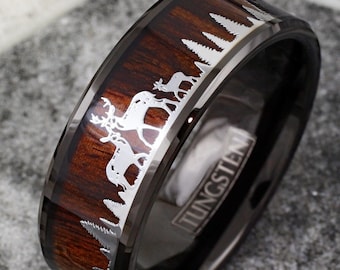 May include: A black tungsten ring with a brown wood inlay and a silver deer silhouette design. The ring is engraved with the word "TUNGSTEN".