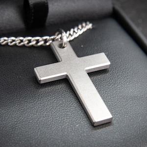 May include: A silver cross pendant on a silver chain necklace. The necklace is in a black velvet box.