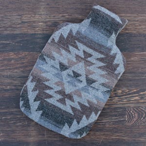 Può includere: Una fodera per borsa dell'acqua calda con motivo grigio, marrone e nero con un design geometrico.