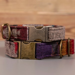 Puede incluir: Dos collares para perros con tela estampada y hebillas metálicas. El collar superior es gris y marrón con una hebilla plateada. El collar inferior es morado, rojo y naranja con una hebilla dorada.