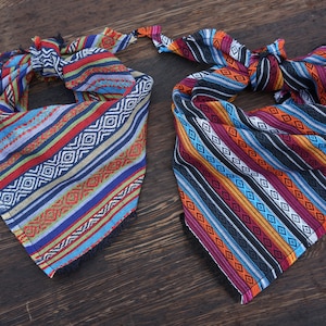 May include: Two colorful bandanas with geometric patterns in shades of blue, red, orange, yellow, and black. The bandanas are made of woven fabric and have fringed edges.