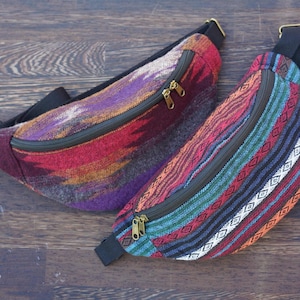 Puede incluir: Dos riñoneras de tejido tejido de colores con correas ajustables y cierres de cremallera. Las riñoneras están sobre una superficie de madera.