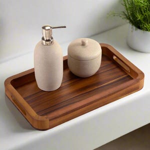 May include: A wooden tray with a natural finish and rounded edges. The tray has two handles and features a beige soap dispenser and a beige container with a lid.