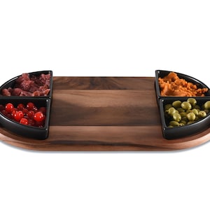 May include: A wooden serving tray with four black ceramic bowls. The bowls contain various foods, including red berries, olives, and a reddish-orange spread. The tray is oval-shaped and made of dark wood.