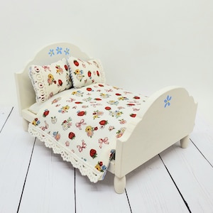May include: A miniature cream-colored bed with a floral strawberry pattern on the bedding and pillows. The bed frame has a scalloped headboard and footboard, with blue flower accents. The bedding is trimmed with a white lace.