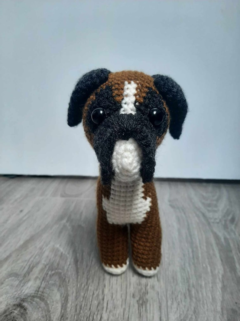 Op de afbeelding: Een bruin en wit gehaakt boxerhond knuffeldier met zwarte oren en zwarte ogen.
