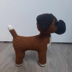 Op de afbeelding: Een gehaakt boxerhondje speelgoed in bruin en wit. De hond staat op een houten vloer.