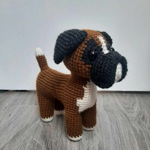 Op de afbeelding: Een gehaakt boxerhondenspeelgoed in bruin en zwart met witte accenten. De hond heeft zwarte ogen en een witte vlek op zijn borst.
