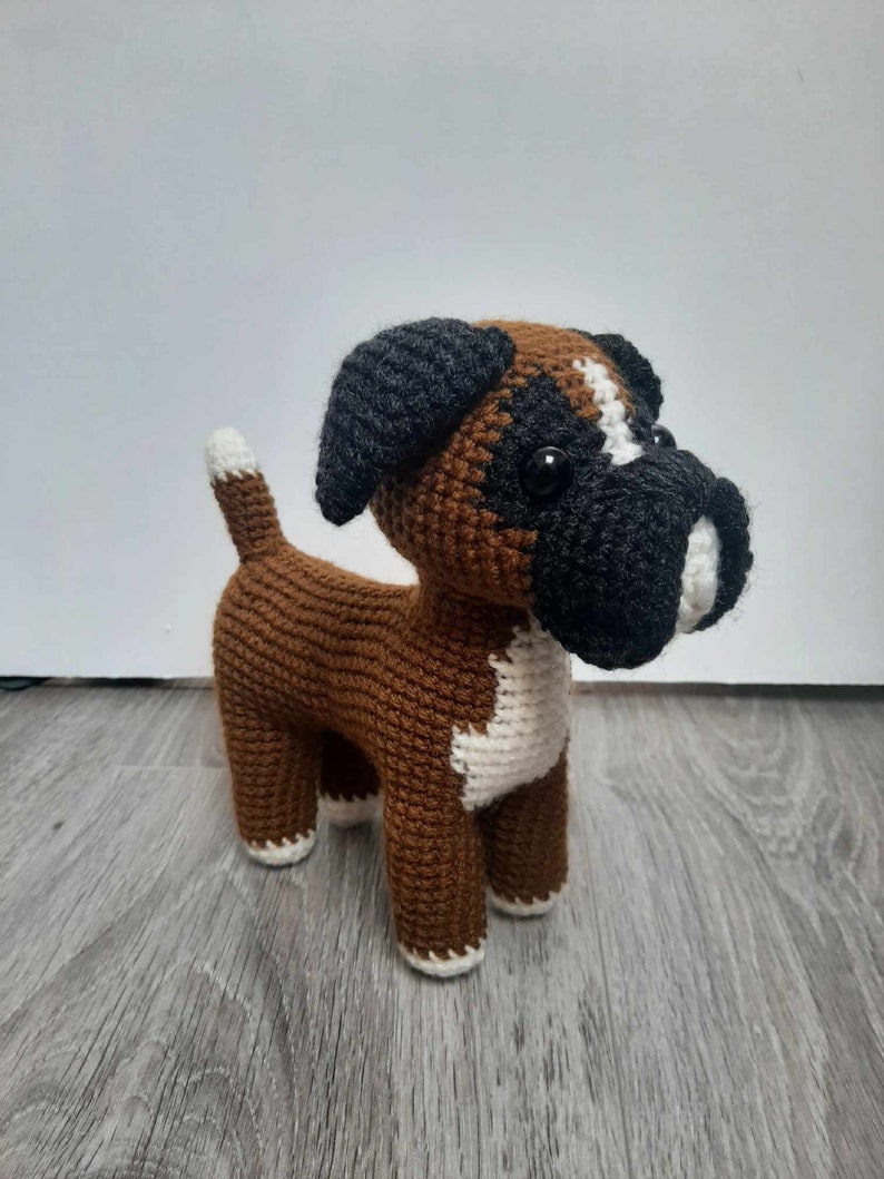Op de afbeelding: Een gehaakt boxerhondenspeelgoed in bruin en zwart met witte accenten. De hond heeft zwarte ogen en een witte vlek op zijn borst.