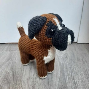 Op de afbeelding: Een gehaakt boxerhondje speelgoed in bruin en wit met zwarte oren en neus. Het speelgoed heeft grote zwarte ogen en een witte vlek op de borst.