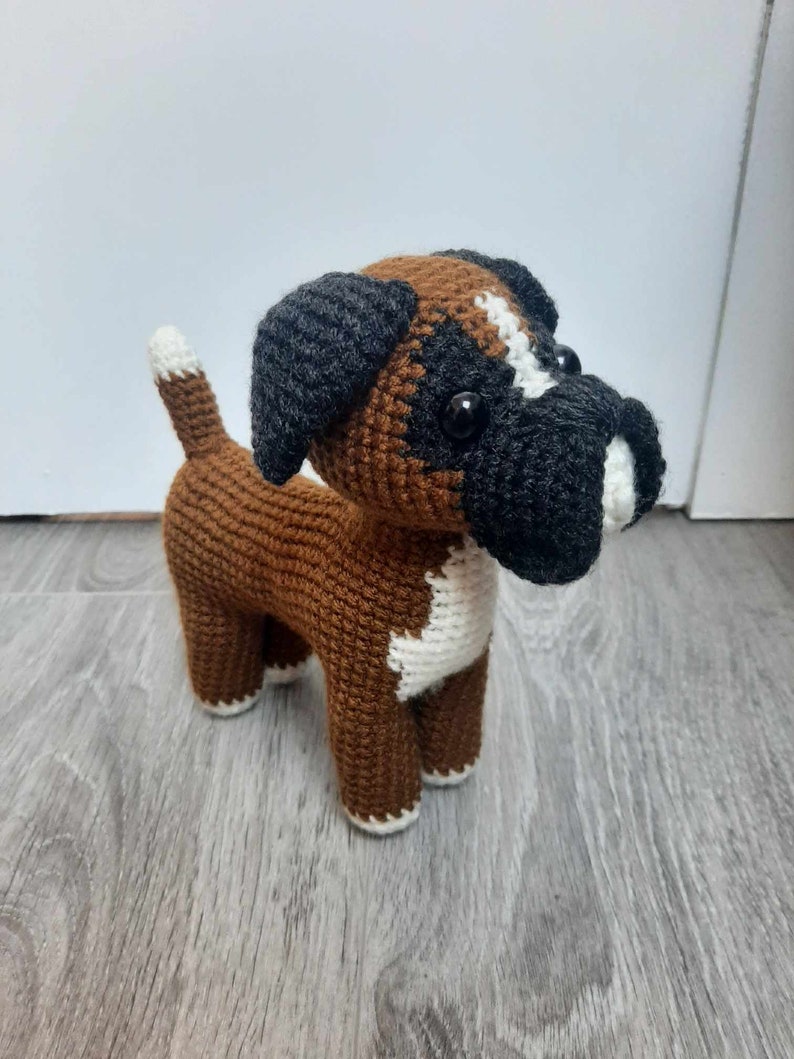 Op de afbeelding: Een gehaakt boxerhondje speelgoed in bruin en wit met zwarte oren en neus. Het speelgoed heeft grote zwarte ogen en een witte vlek op de borst.