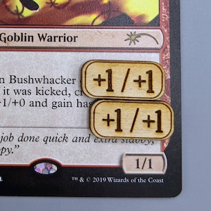 May include: A red, white, and black Magic: The Gathering card featuring a goblin warrior with a sword and a shield. The card text reads "Goblin Bushwhacker" and "Creature - Goblin Warrior".