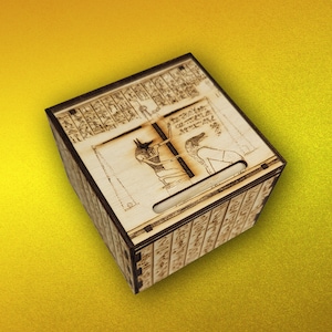 May include: A wooden box with an intricate design of Egyptian hieroglyphs and a depiction of Anubis and a jackal. The box has a slot on the side.