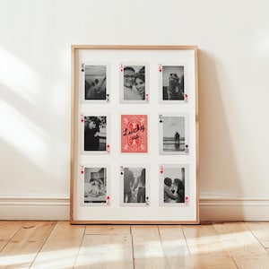 May include: A framed wall art piece featuring playing card designs with black and white photographs. The central card is red with the text "Lucky us." The frame is a light brown color.