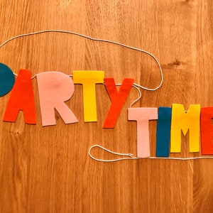 May include: A felt banner with the words "PARTY TIME" in colorful letters. The letters are strung together with white string and are in the colors blue, red, pink, yellow, and orange.