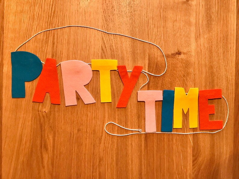 May include: A felt banner with the words "PARTY TIME" in colorful letters. The letters are strung together with white string and are in the colors blue, red, pink, yellow, and orange.