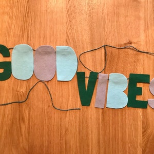 May include: A felt banner with the words "GOOD VIBES" in green letters, with alternating light blue and purple felt pieces between the letters.
