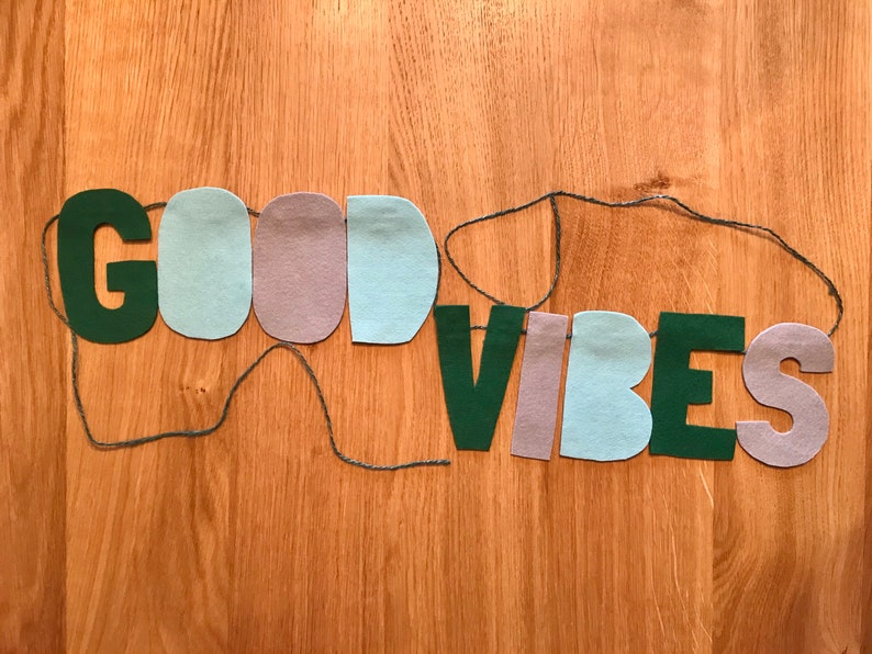 May include: A felt banner with the words "GOOD VIBES" in green letters, with alternating light blue and purple felt pieces between the letters.