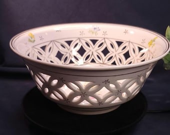 Peut inclure: Un bol en céramique blanc avec un motif ajouré décoratif. Le bol présente un motif floral sur le bord et des découpes géométriques. Le bol est posé sur une surface noire.