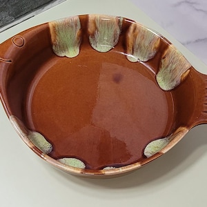 May include: A brown ceramic fish-shaped baking dish with a green and white glaze. The dish has a handle on the side and a raised lip around the edge.