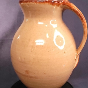 Può includere: Una brocca in ceramica con corpo arrotondato e manico curvo. La brocca è di colore pesca chiaro con bordo e dettagli del manico marrone scuro. La brocca viene probabilmente utilizzata per servire bevande.
