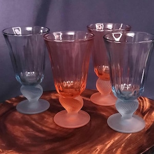 Könnte beinhalten: Vier Vintage-Stielgläser mit einem einzigartigen Design. Die Gläser haben eine klare Schale, einen mattierten, gewirbelten Stiel und einen farbigen Fuß. Zwei Gläser sind blau und zwei rosa, was ein farbenfrohes und elegantes Set ergibt.