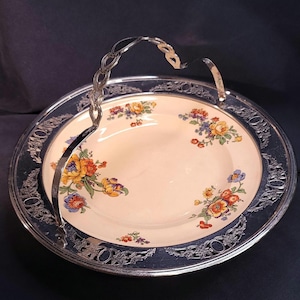 May include: A vintage serving tray with a floral patterned plate and a silver-toned handle. The plate features colorful flowers in shades of yellow, orange, and purple. The tray has a decorative silver rim.