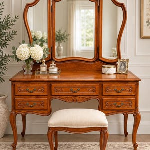 May include: A wooden vanity table with a tri-fold mirror and five drawers, featuring curved legs and ornate metal pulls. A matching upholstered stool with a beige seat and curved wooden legs is positioned in front of the vanity.