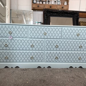 May include: A light blue chest of drawers with six drawers. The drawers have a geometric pattern and gold handles.