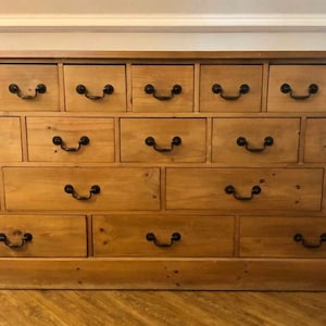 May include: A wooden dresser with 18 drawers and black metal handles. The dresser is made of light brown wood and has a simple design.