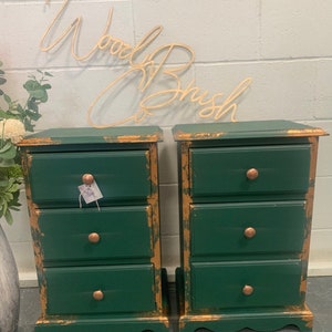 May include: Two green painted bedside tables with three drawers each. The drawers have gold accents and copper coloured knobs. The bedside tables are distressed and have a rustic look.