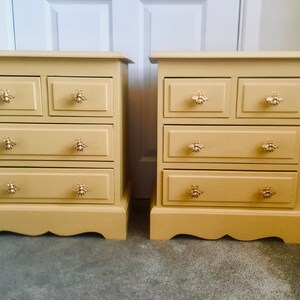 May include: Two yellow painted wooden bedside tables with four drawers each. The drawers have bee-shaped handles.