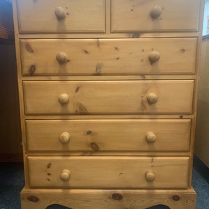May include: A wooden chest of drawers with six drawers and rounded knobs. The chest of drawers is made of light brown wood and has a scalloped base.
