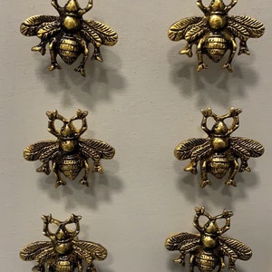 May include: Six gold-toned bee-shaped drawer pulls. Each pull features a detailed design with wings, legs, and a textured body.