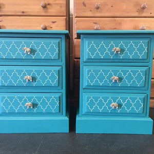 May include: Two teal blue bedside tables with three drawers each. The drawers have white geometric patterns and silver elephant-shaped knobs.