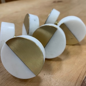 May include: Five round white marble and gold cabinet knobs. Each knob is half white marble and half gold metal.