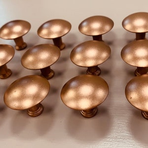 May include: A set of 12 gold-toned cabinet knobs with a round, slightly domed shape. The knobs have a smooth, metallic finish.