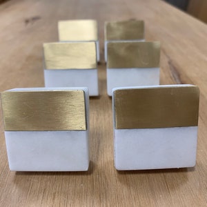 May include: Six square cabinet knobs with a white marble base and a gold top.