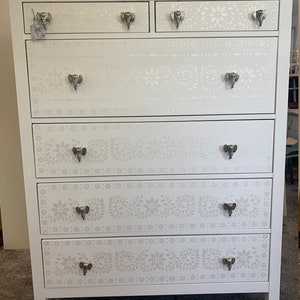 May include: White chest of drawers with six drawers featuring an intricate floral and elephant design. Each drawer has a silver elephant-shaped knob.