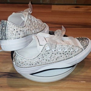 May include: A pair of white canvas sneakers with a white ribbon and embellished with white pearls and rhinestones.