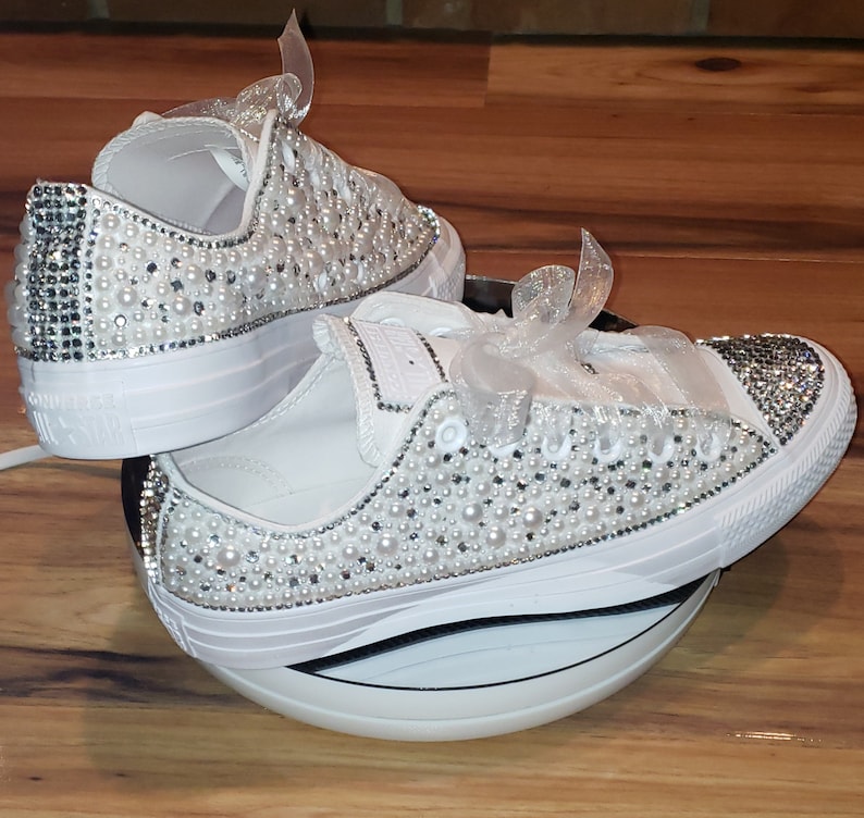 May include: A pair of white canvas sneakers with a white ribbon and embellished with white pearls and rhinestones.