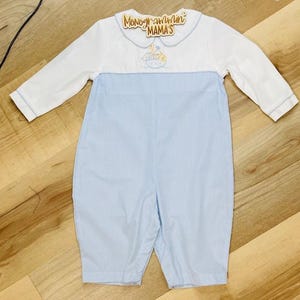 May include: A baby romper with a white top and light blue striped bottom. The romper has long sleeves with light blue trim and a Peter Pan collar. The collar has the text "Monogrammin' MAMA'S".