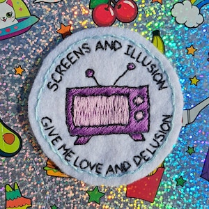 Könnte beinhalten: Gestickter Aufnäher mit hellblauem Hintergrund und einem lila Fernsehdesign. Der Aufnäher zeigt den Text "SCREENS AND ILLUSION GIVE ME LOVE AND DELUSION" in einem kreisförmigen Muster um den Fernseher.